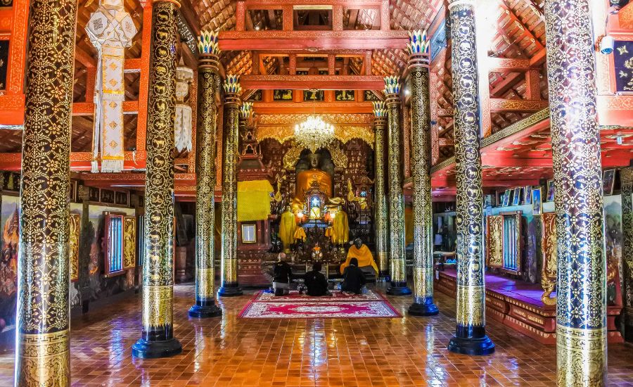 Intricate Lanna-style wooden interior and golden pillars inside a Northern Thai temple