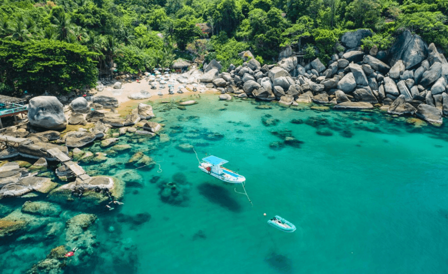 Tropical Thai bay with turquoise water, green cliffs, and granite boulders