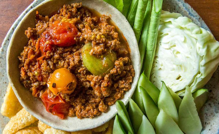 A bowl of Nam Prik Ong served with fresh vegetables and pork rinds